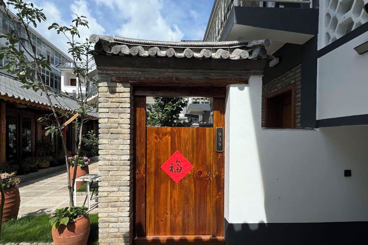Une porte en bois traditionnelle, avec une enseigne rouge, un mur de briques et, au fond, un bâtiment moderne.