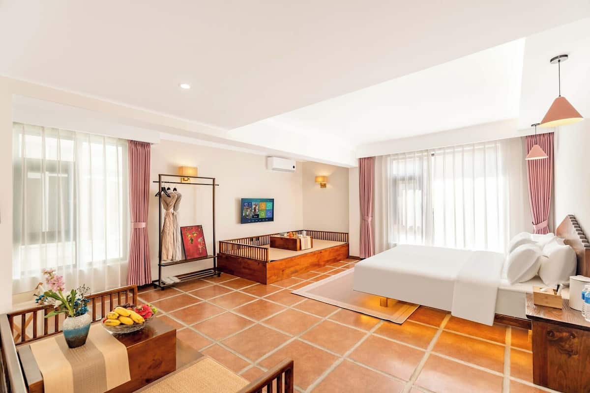 Une chambre d’hôtel moderne dotée d’un grand lit, d’un coin salon avec une table et des chaises, d’un petit canapé et d’un téléviseur fixé au mur.