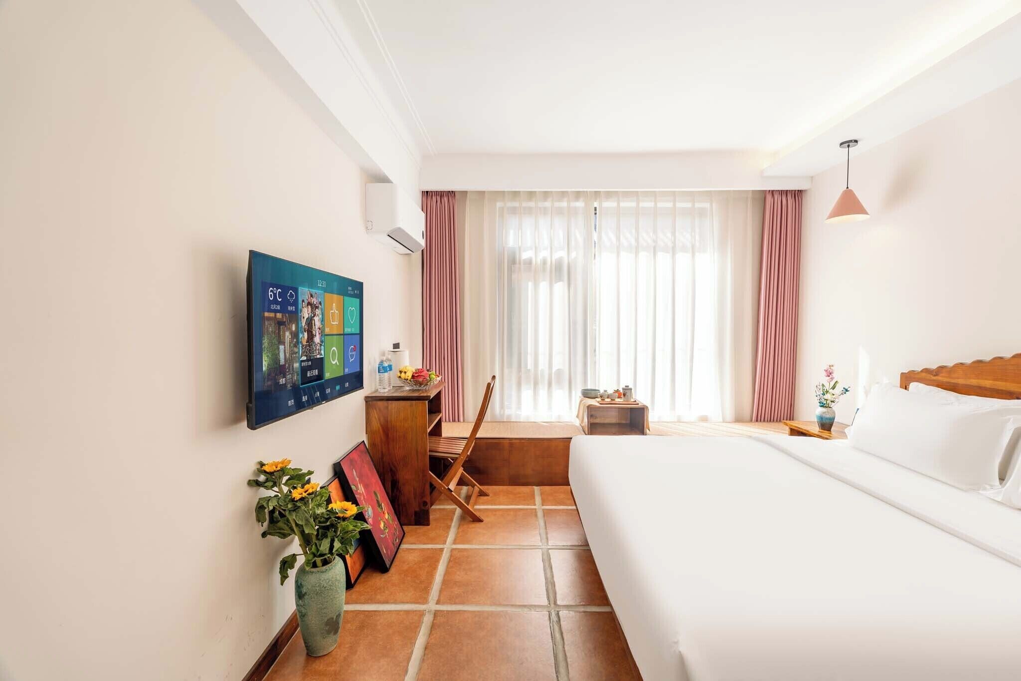 A hotel room with a bed, a desk, a chair, a TV mounted on the wall, and a window with curtains.