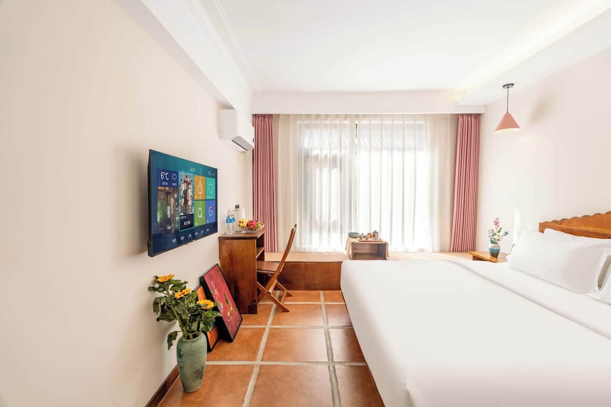 Une chambre d’hôtel équipée d’un lit, d’un bureau, d’une chaise, d’un téléviseur fixé au mur et d’une fenêtre avec des rideaux.