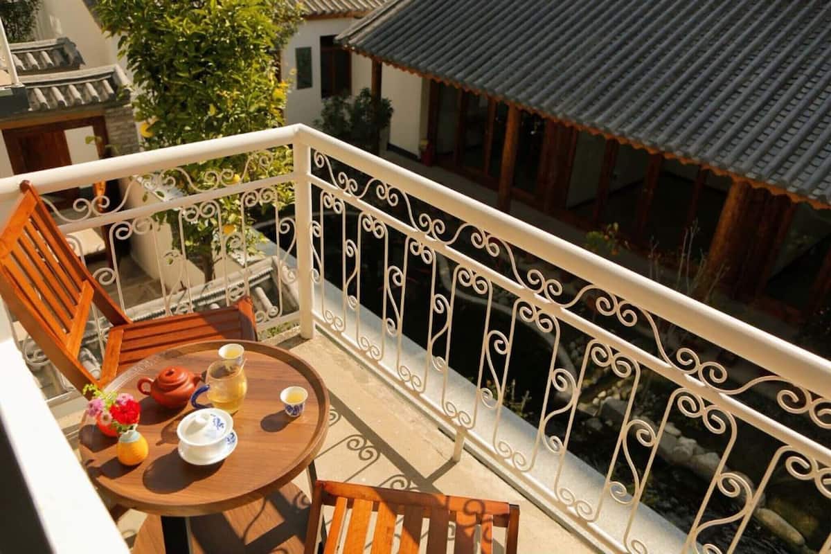 Un balcon avec une table ronde en bois, deux chaises, une théière, une tasse et un vase rempli de fleurs.