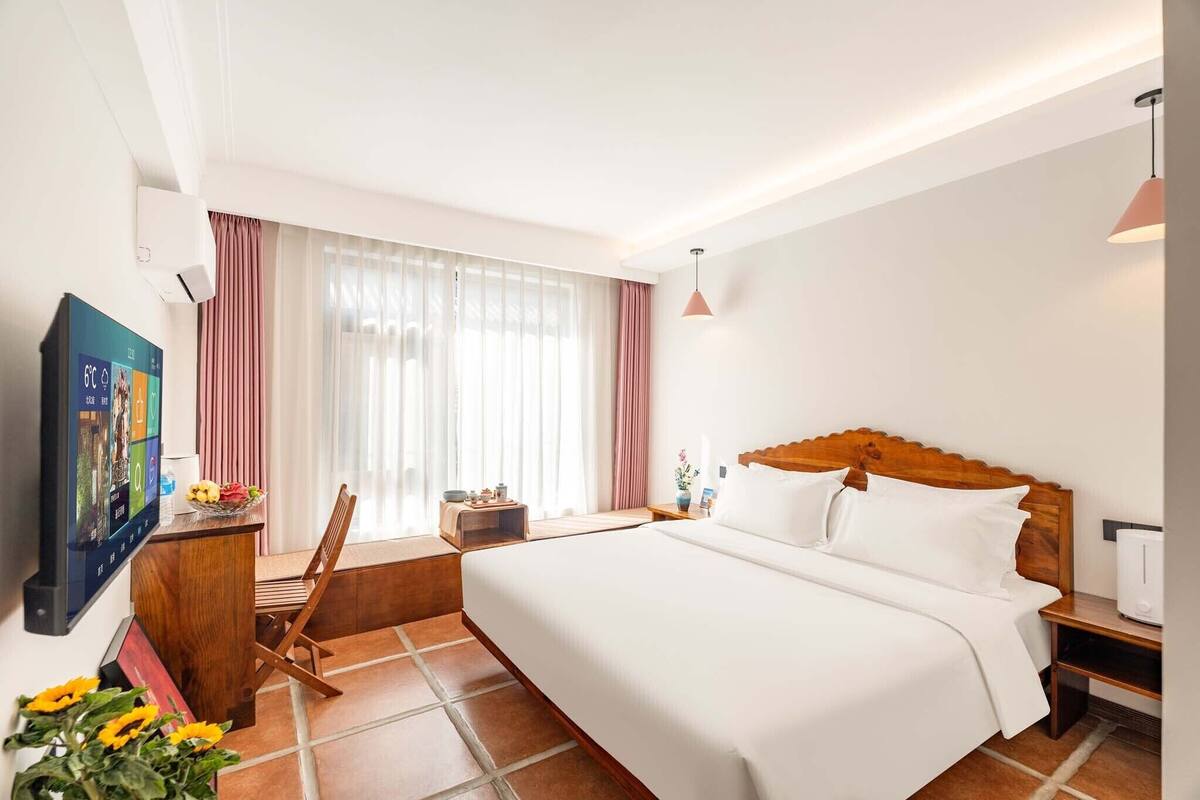 Une chambre d’hôtel comprenant un lit, un bureau avec un ordinateur, une chaise, une fenêtre avec des rideaux et un climatiseur fixé au mur.