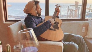 A person playing a guitar on a couch with a view of the ocean through large windows. - Native Residence Casa 4 (Playas de Rosarito)