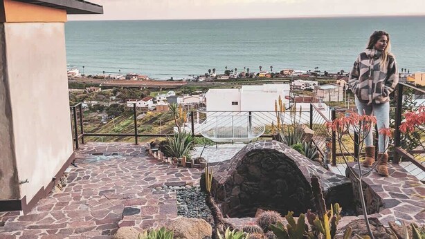 A terrace with a stone floor, a white chair, and a view of the sea and town. - Native Residence Casa 4 (Playas de Rosarito)