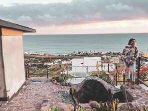 A terrace with a stone floor, a white chair, and a view of the sea and town. - Native Residence Casa 4 (Playas de Rosarito)