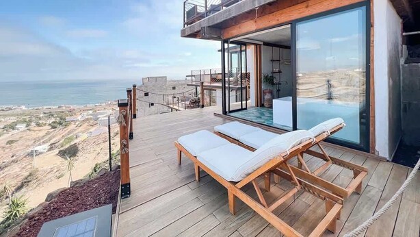 Eine moderne Außenterrasse mit Liegestühlen, einem gläsernen Infinity-Pool und Blick auf die Küste.