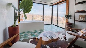 Ein modernes Zimmer mit großem Fenster, einer Badewanne, einem runden Holztisch und einem Sessel.