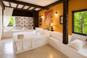 A bedroom with a large bed, a window with curtains, a painting, and a lamp.