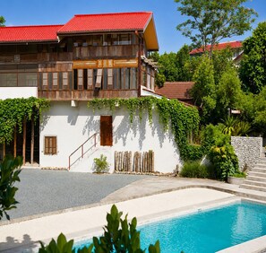 A two-story building with a red-tiled roof, a swimming pool, and a stone wall. - Hacienda Isabella Garden Resort (Indang)