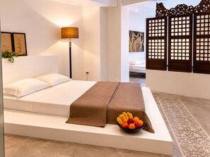 A modern bedroom with a bed, a bedside lamp, a decorative screen, and a bowl of fruit on the bed.