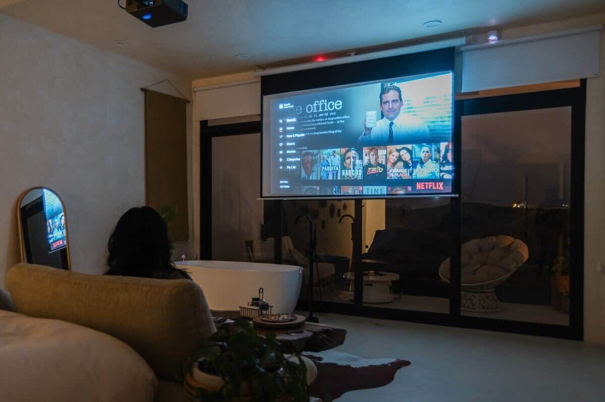 A modern living room with a large flat-screen TV displaying a streaming service interface, a sofa, a coffee table, and a glass door leading to a balcony.