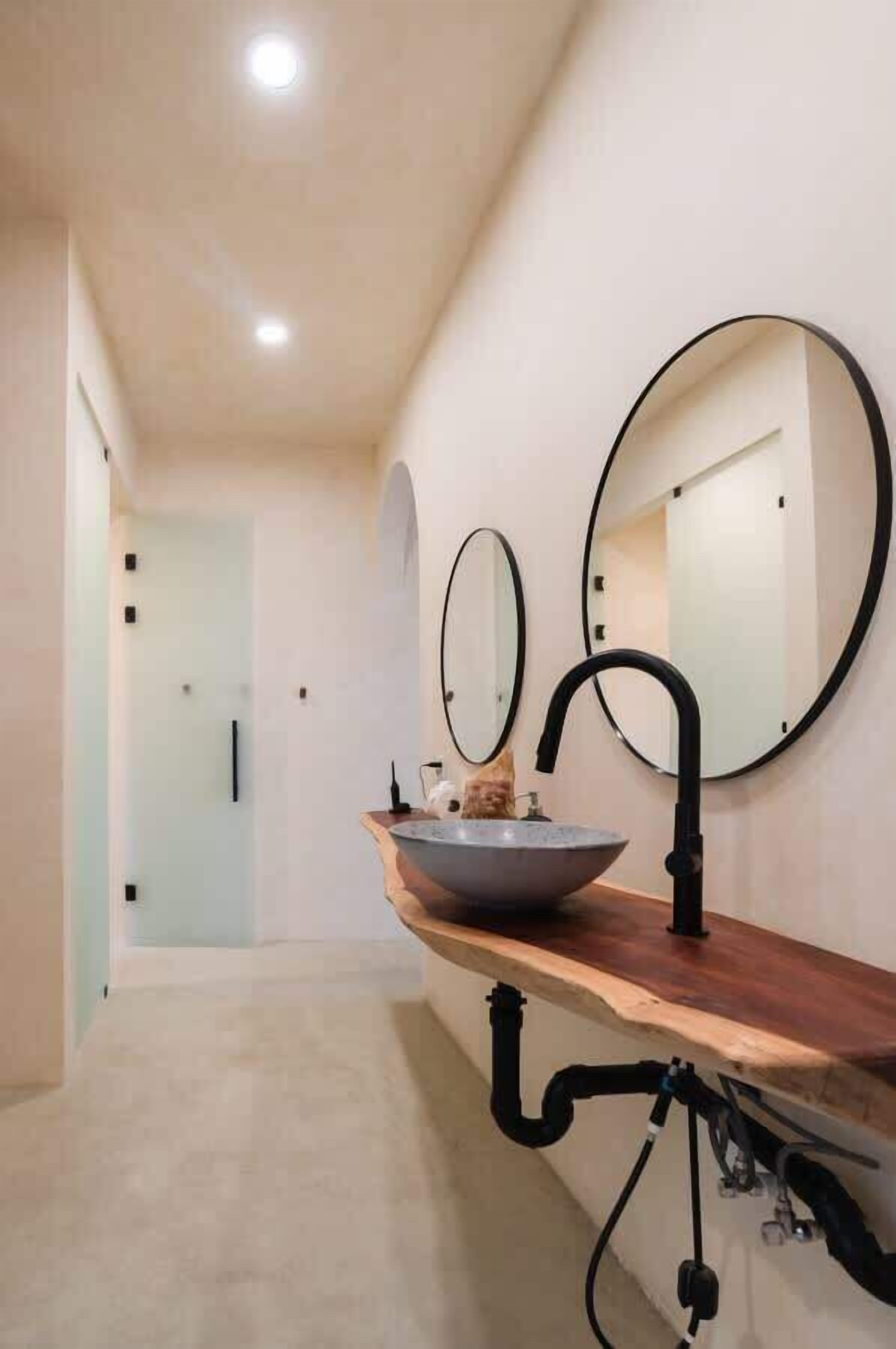 Un baño moderno con tocador de madera, un lavabo sobre encimera y dos espejos redondos colgados en la pared.