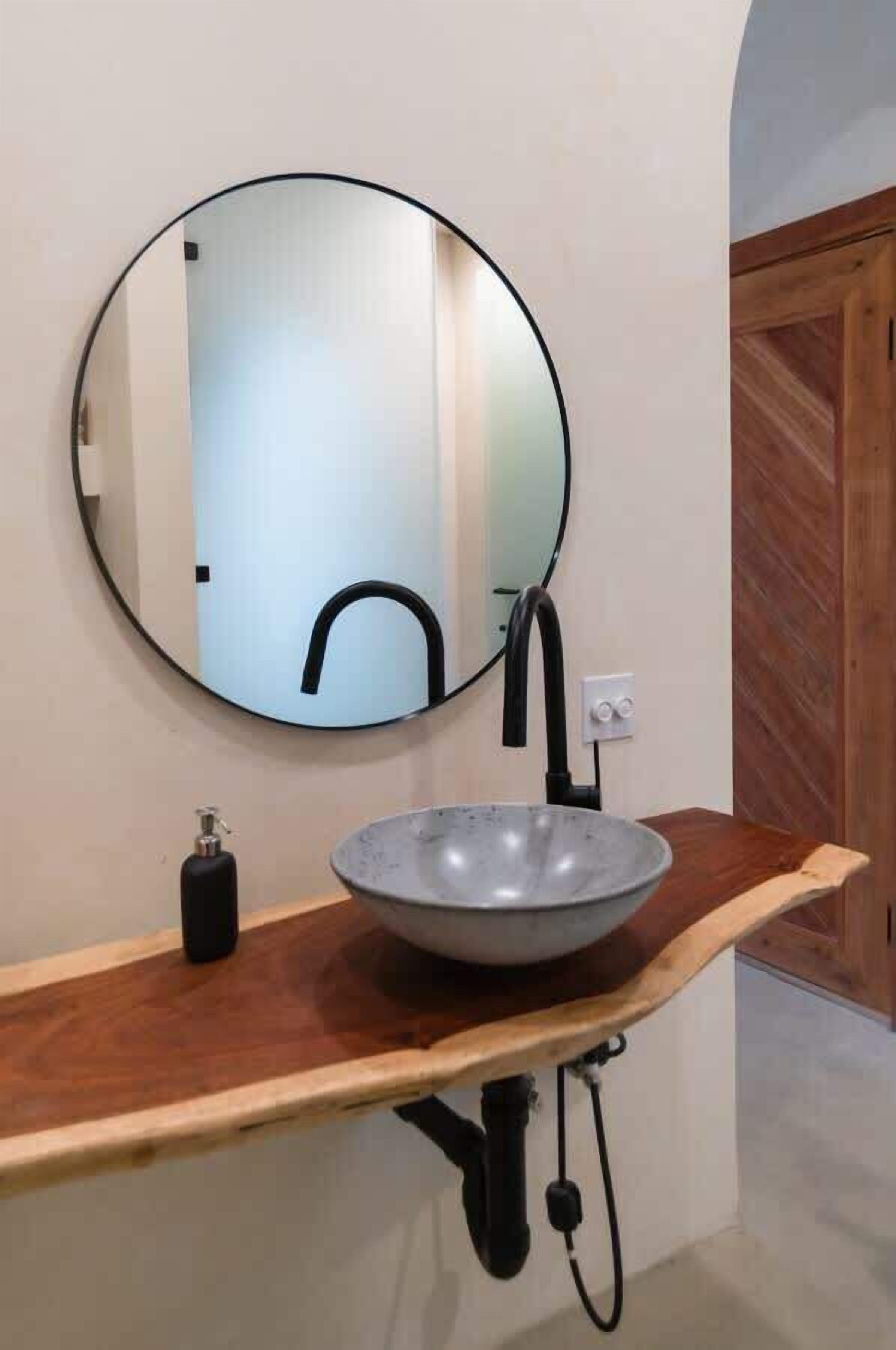 A bathroom with a round mirror, a vessel sink, and a wooden countertop.