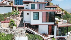 Uma casa moderna de dois andares, com base de pedra, grandes janelas e uma varanda.