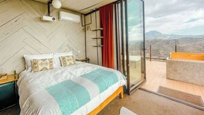 Quarto com uma cama grande, porta de vidro deslizante para uma varanda e vista para as montanhas.