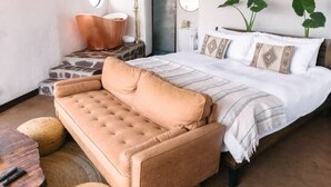 A bedroom with a bed, a sofa, a wooden table, and a hanging light fixture. - Native Residence Casa 6 (Playas de Rosarito)