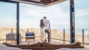 Quarto com cama grande, sofá e varanda com vista.