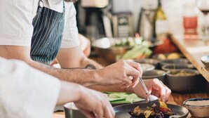 Uno chef che prepara cibo in cucina, con diversi utensili e ingredienti sul bancone.