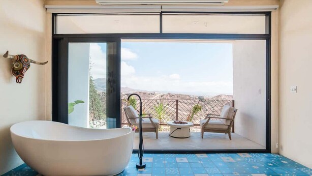 Un bagno moderno con una vasca freestanding, una doccia e un'ampia porta scorrevole in vetro che dà su un balcone con mobili da esterno.