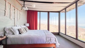 Une chambre à coucher moderne avec un grand lit, un rideau rouge et une vue sur le désert, visible à travers de grandes fenêtres.