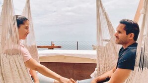 Um casal sentado em uma rede numa varanda com vista para uma ponte.