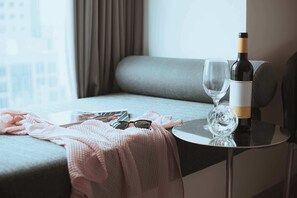Hotelkamer met een bank, een kleine tafel met een fles wijn en een glas, en een raam met gordijnen.