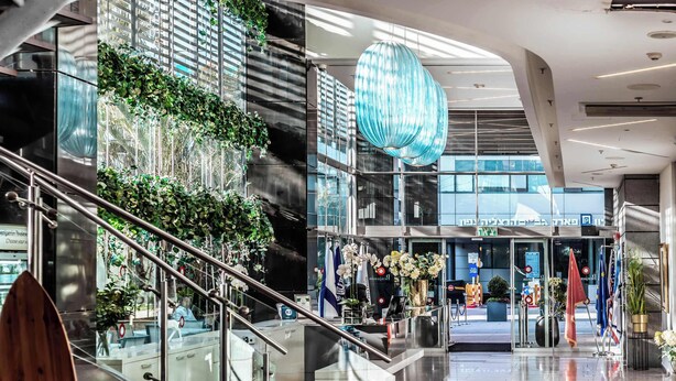 Un moderno vestíbulo de hotel con una escalera de cristal, plantas de interior y una gran lámpara esférica azul.