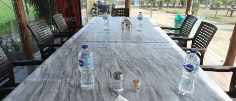 Una mesa de mármol con botellas de agua, saleros y pimenteros, rodeada de sillas en una habitación con ventanas amplias.