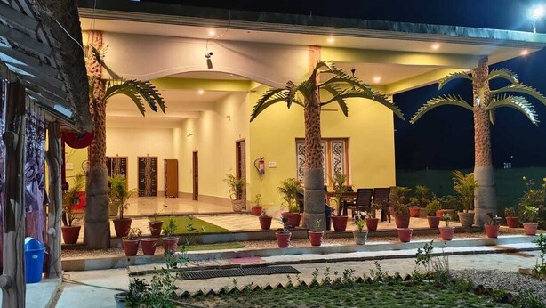 A hotel with a covered outdoor area, palm trees, and potted plants. - Royal Chuka Farm Stay (Puranpur)