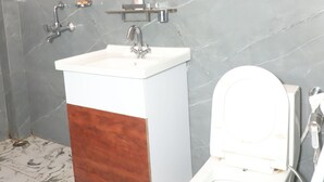 A bathroom with a marble floor, a white sink with a wooden panel, a toilet, and a mirror with a towel hanging on the wall. - Royal Chuka Farm Stay (Puranpur)