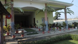 A building with a covered entrance, palm trees, and potted plants. - Royal Chuka Farm Stay (Puranpur)