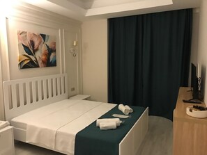 Ein Hotelzimmer mit Bett, Nachttisch, einem Gemälde, einer Lampe, einem Fernseher und einem dunklen Vorhang.