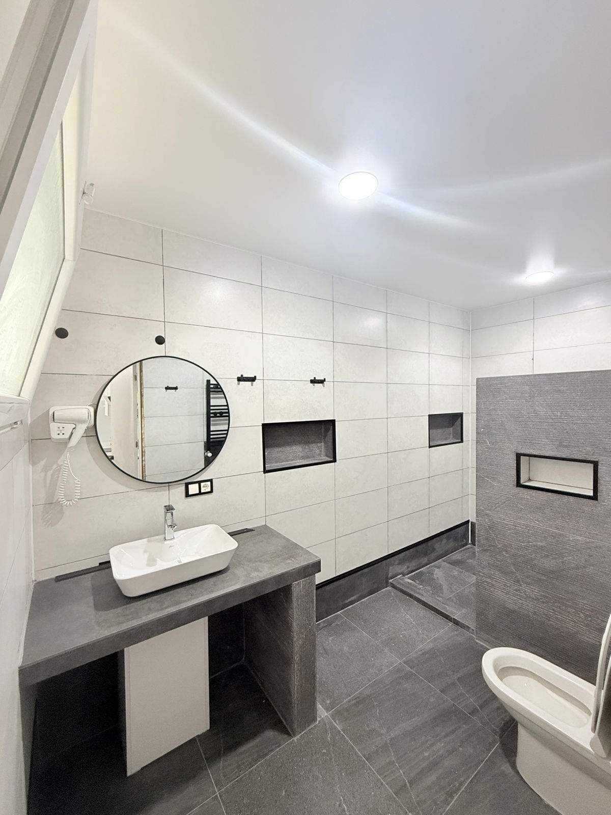 A modern bathroom with a white sink, a round mirror, a toilet, and a shower area.