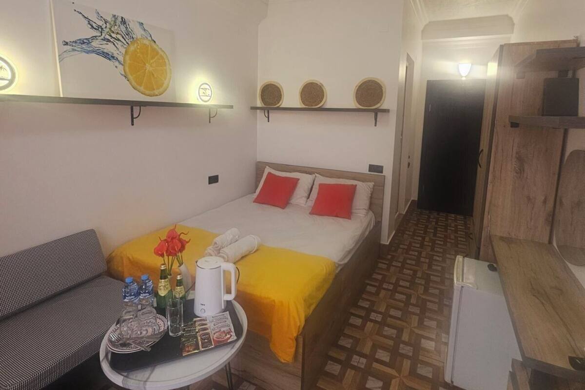 Een kleine, knusse kamer met een bed, een bank, een tafel met een dienblad met toiletartikelen, en een wandplank met decoratieve borden.