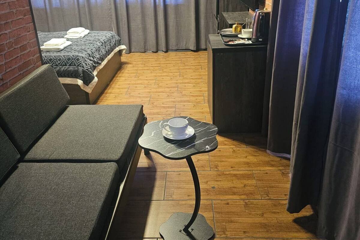 Een knus hotelkamer met een bed, een slaapbank, een klein tafeltje met een kopje en een houten vloer.