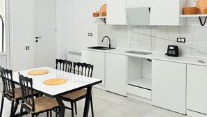 Une cuisine moderne avec des meubles blancs, une table à manger avec des chaises et un luminaire au plafond original.