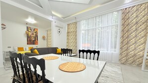 Un salon moderne comprenant un coin repas, un canapé et une grande fenêtre agrémentée de rideaux à motifs.