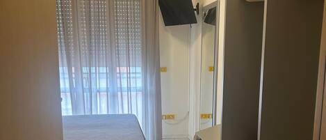 Een hotelkamer met een bed, een bureau, een kledingkast, een aan de muur bevestigde televisie en een raam met gordijnen.