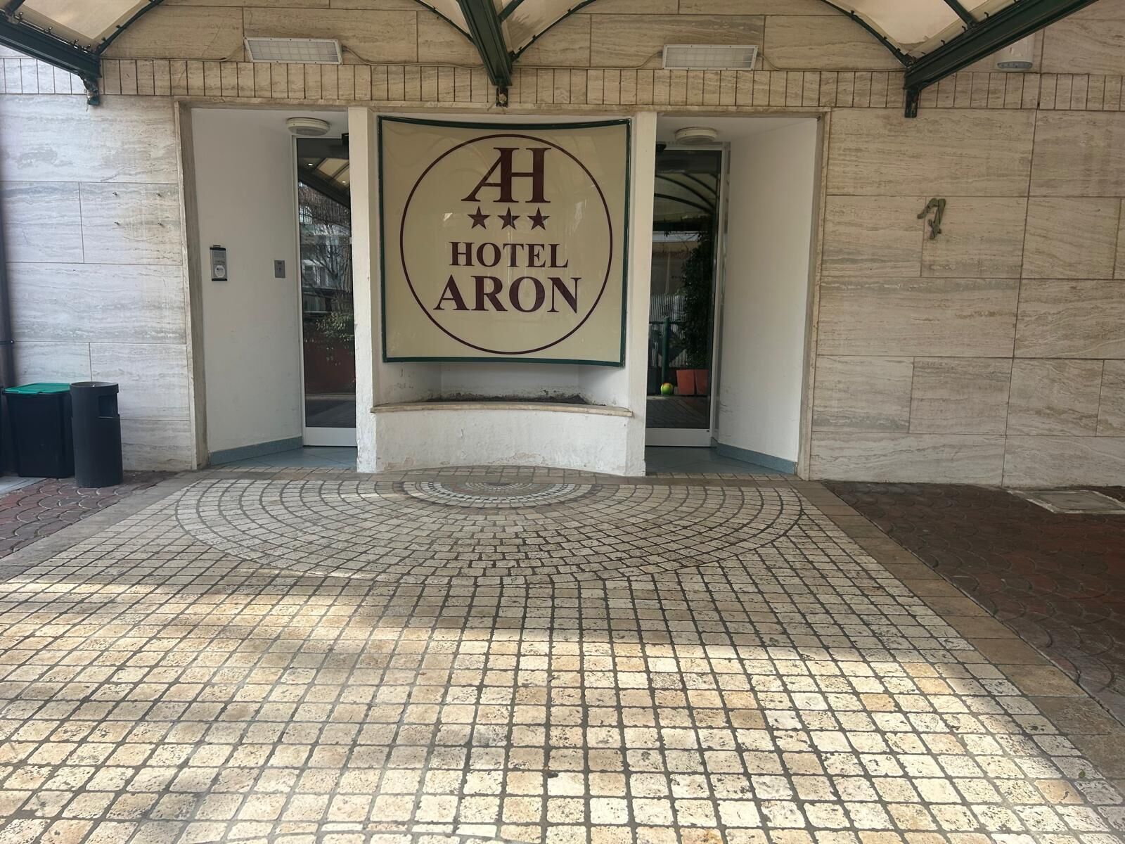 L’entrée d’un hôtel, avec une enseigne indiquant « AH HOTEL ARON » et un sol carrelé.
