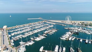 An aerial view of a marina with numerous boats docked, a prominent Ferris wheel, and a coastal backdrop. - Hotel Aron Rimini (Rimini)