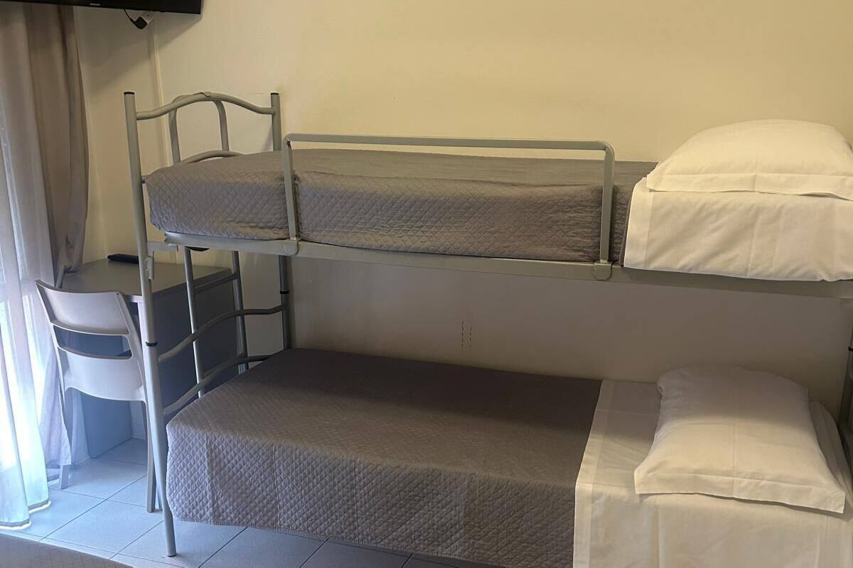 A bunk bed room with a TV mounted on the wall, a chair, and a bed with a quilted cover.