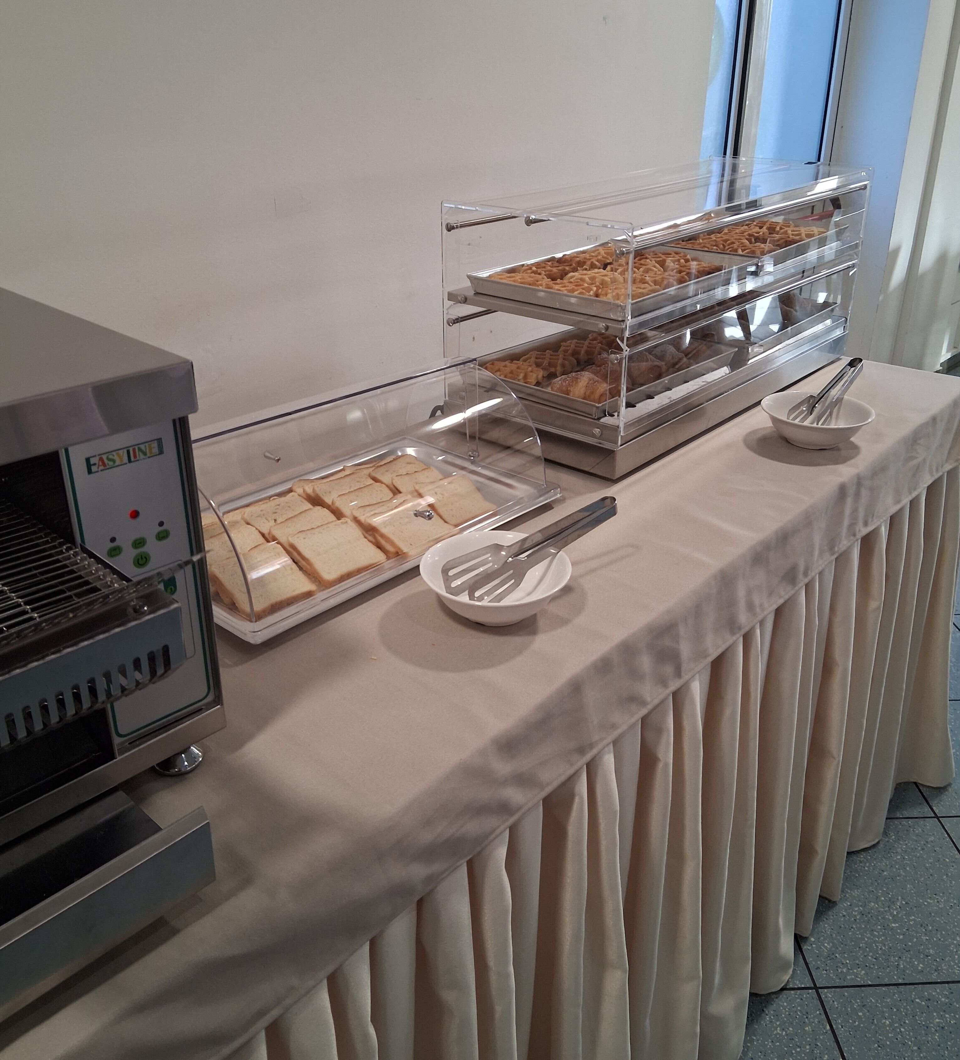 A buffet setup with a sandwich station, a waffle station, and a bread station, all covered with clear plastic.
