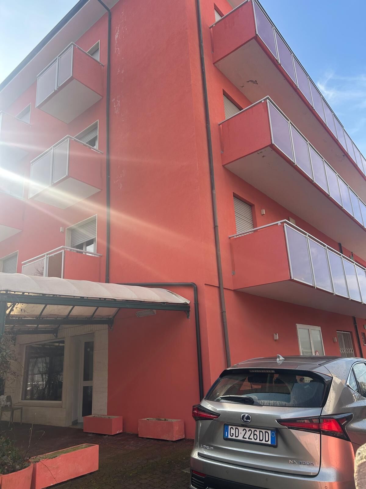 A multi-story building with balconies, a covered entrance, and a parked car.