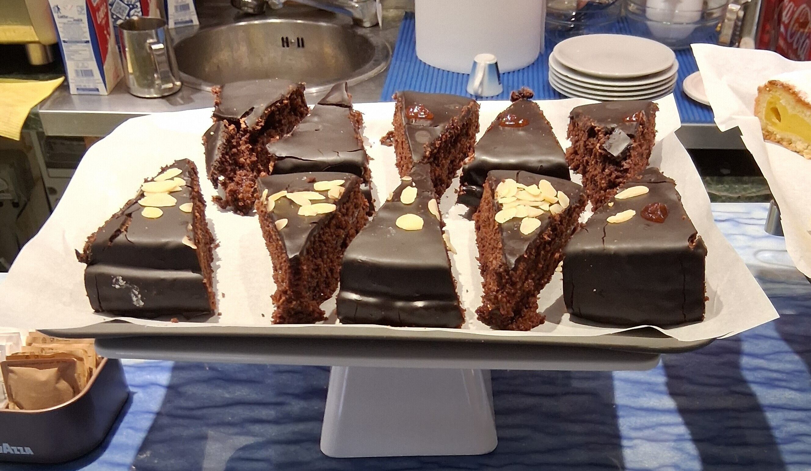 Presentación de rebanadas de pastel cubiertas de chocolate y almendras sobre un soporte blanco.