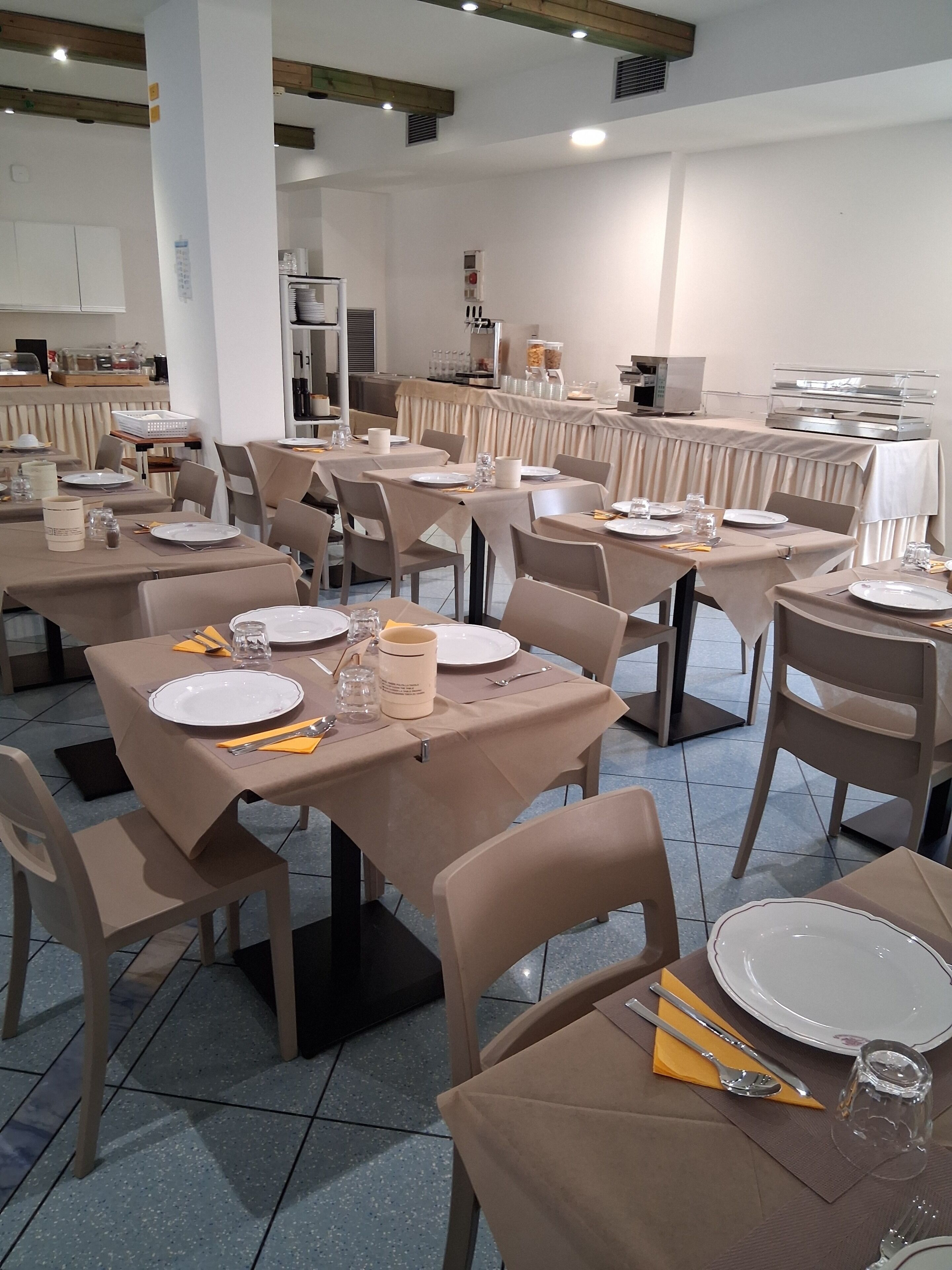 A restaurant with multiple tables set for dining, equipped with plates, cutlery, and glasses.