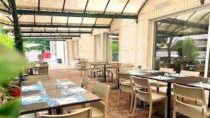 A covered outdoor dining area with tables and chairs, a brick floor, and a glass door leading outside. - Hotel Aron Rimini (Rimini)