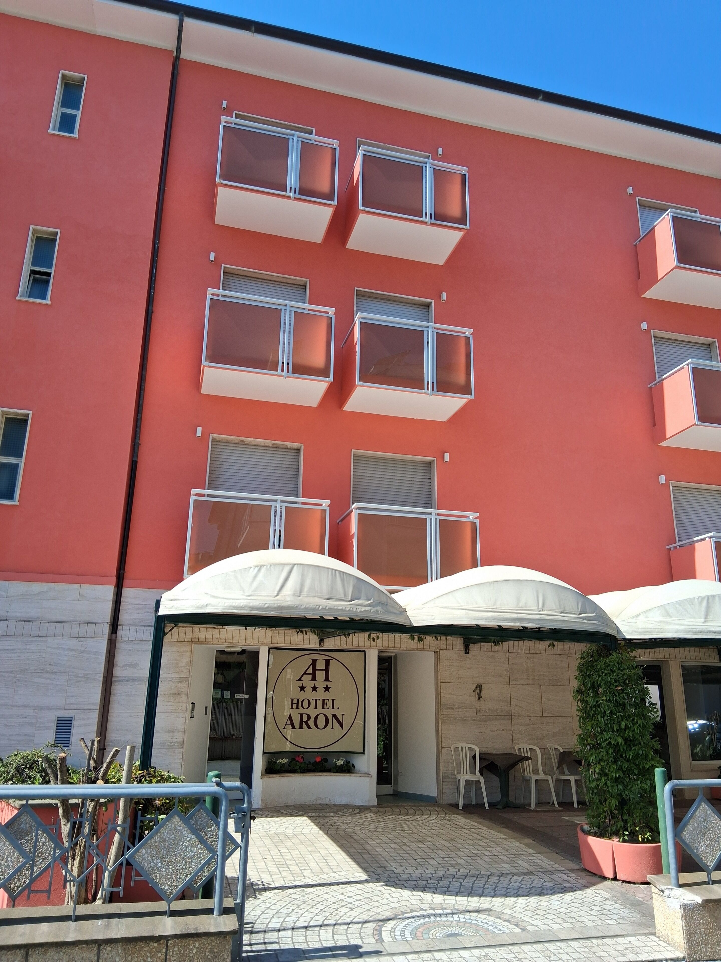A hotel with a red facade, multiple balconies, and outdoor seating with umbrellas.