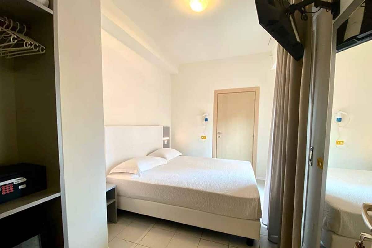 A hotel room with a bed, a wardrobe, a mirror, and a door.
