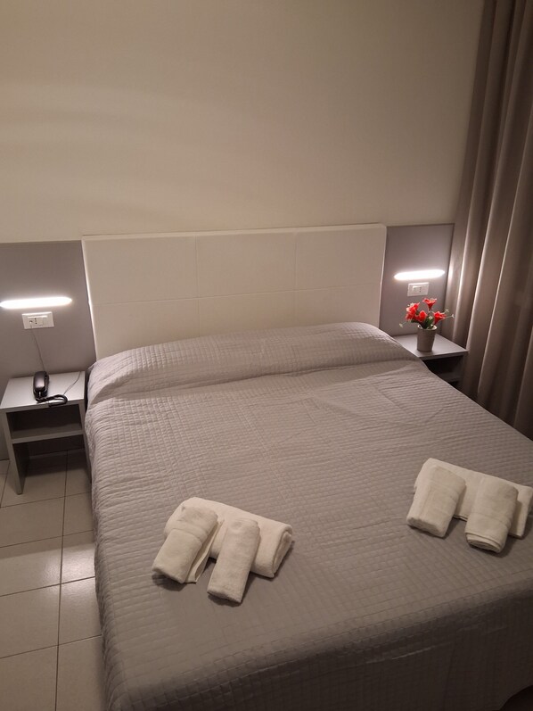 A hotel room with a bed, two bedside tables, a nightstand, a lamp, and a vase with flowers.