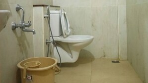 Een badkamer met een toilet, een douche en een grote beige emmer.